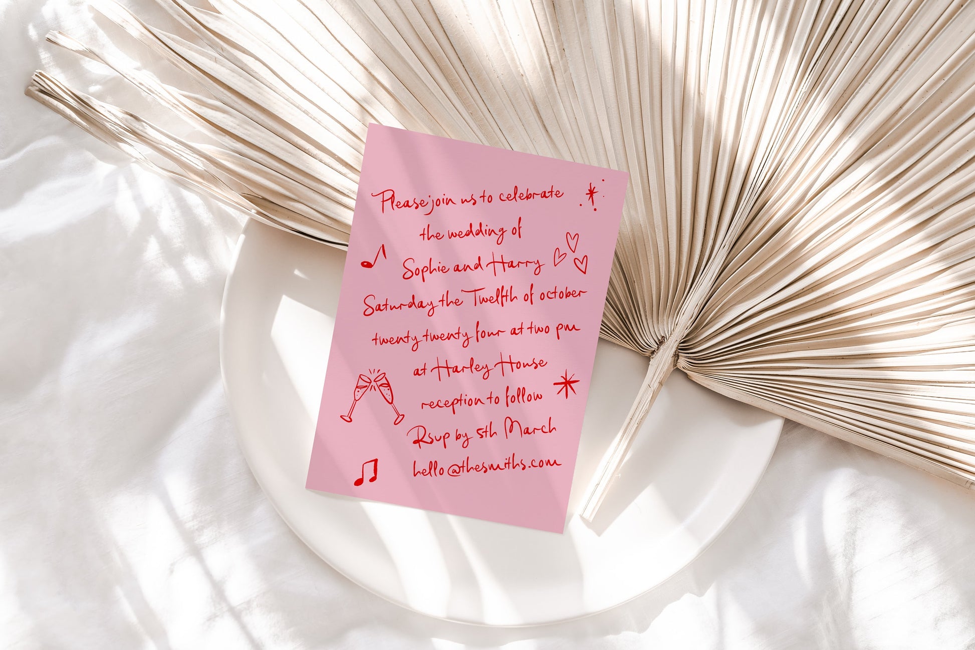 Wedding invite with a pink background and red handwritten font featuring cute doodles